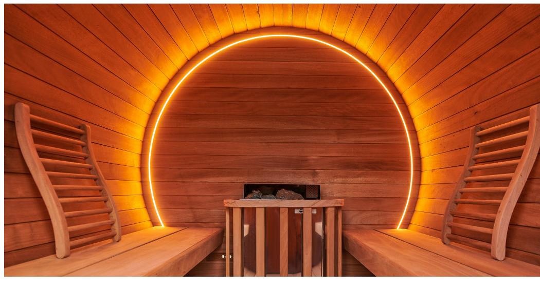 Interior da sauna barril Brasa da EREZ com um arco de luz âmbar emoldurando a parede de madeira.